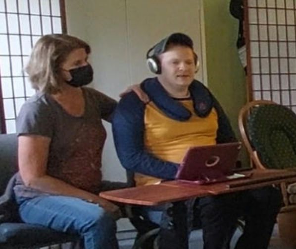 Woman in mask with arm around a man using a tablet, both indoors.