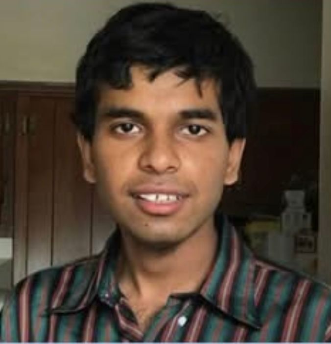 Man with dark hair and a striped shirt smiles at the camera, indoors.