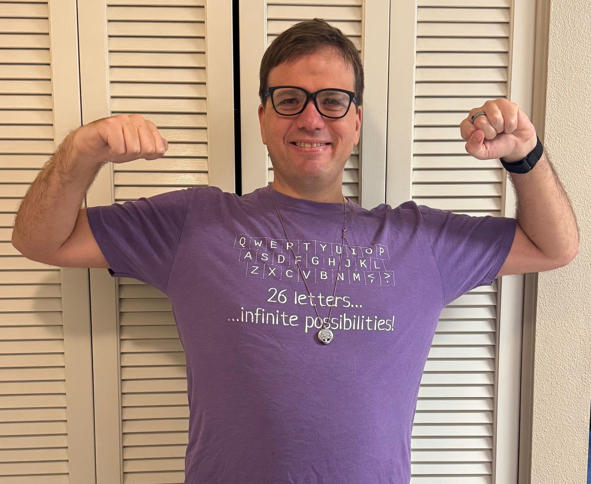 Man flexing arms in purple shirt, glasses, smiling in front of white louvered doors.