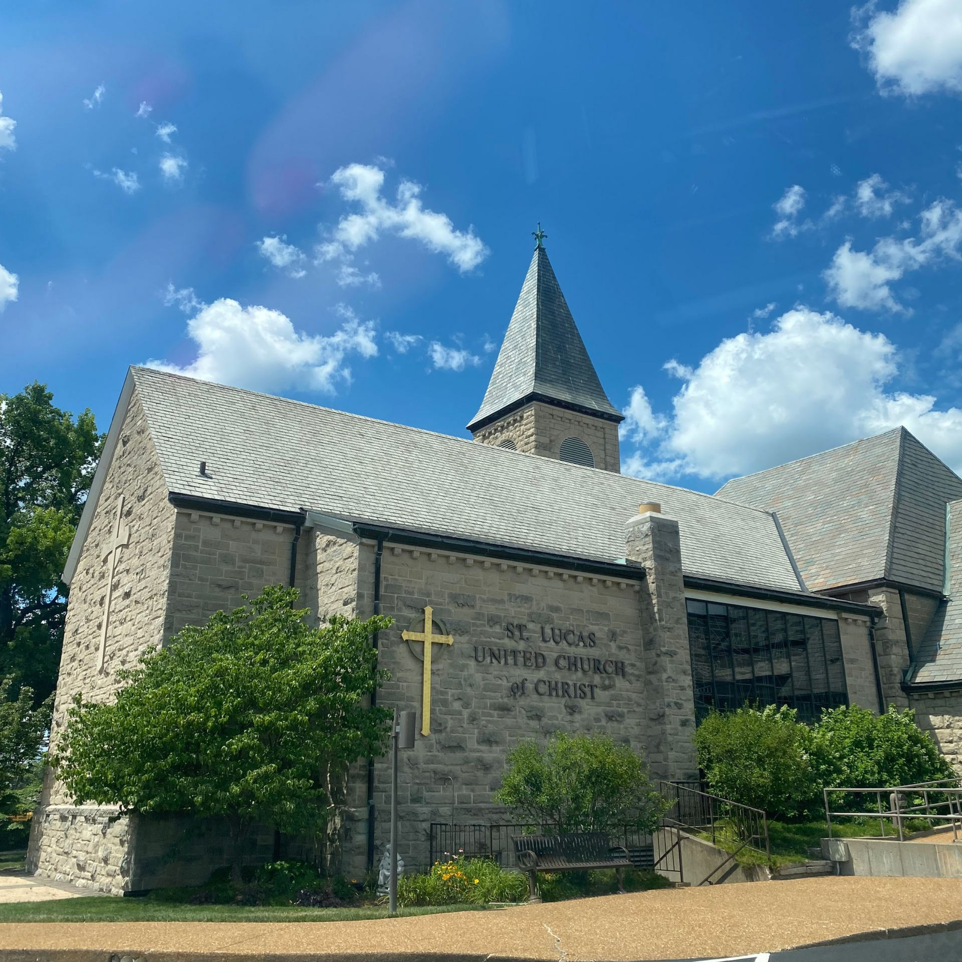 Stone building of St. Lucas United Church of Christ with a steeple under a bright blue sky with scattered clouds.