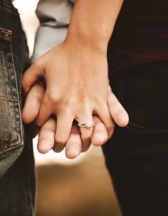 Two people holding hands, one wearing a diamond ring