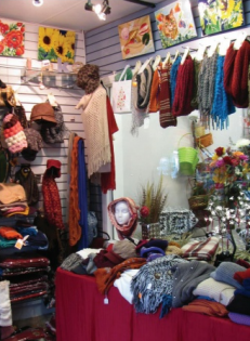 Boutique display with colorful scarves, sweaters, and handmade textiles on shelves and hanging racks