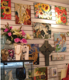 Wall display of colorful floral art, crosses, and fishing decor on slatwall shelves