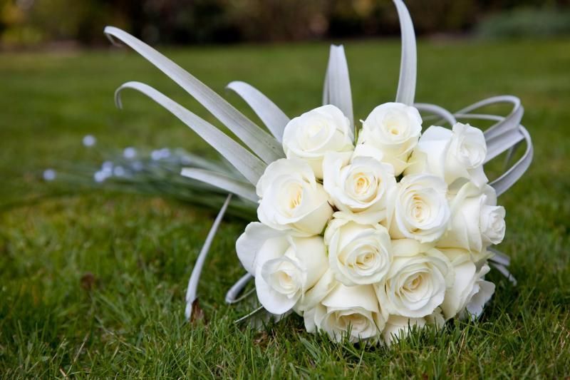 White rose bouquet with decorative ribbons resting on green grass