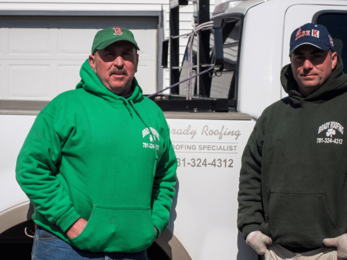 Two men in hoodies standing beside a work truck in front of a garage