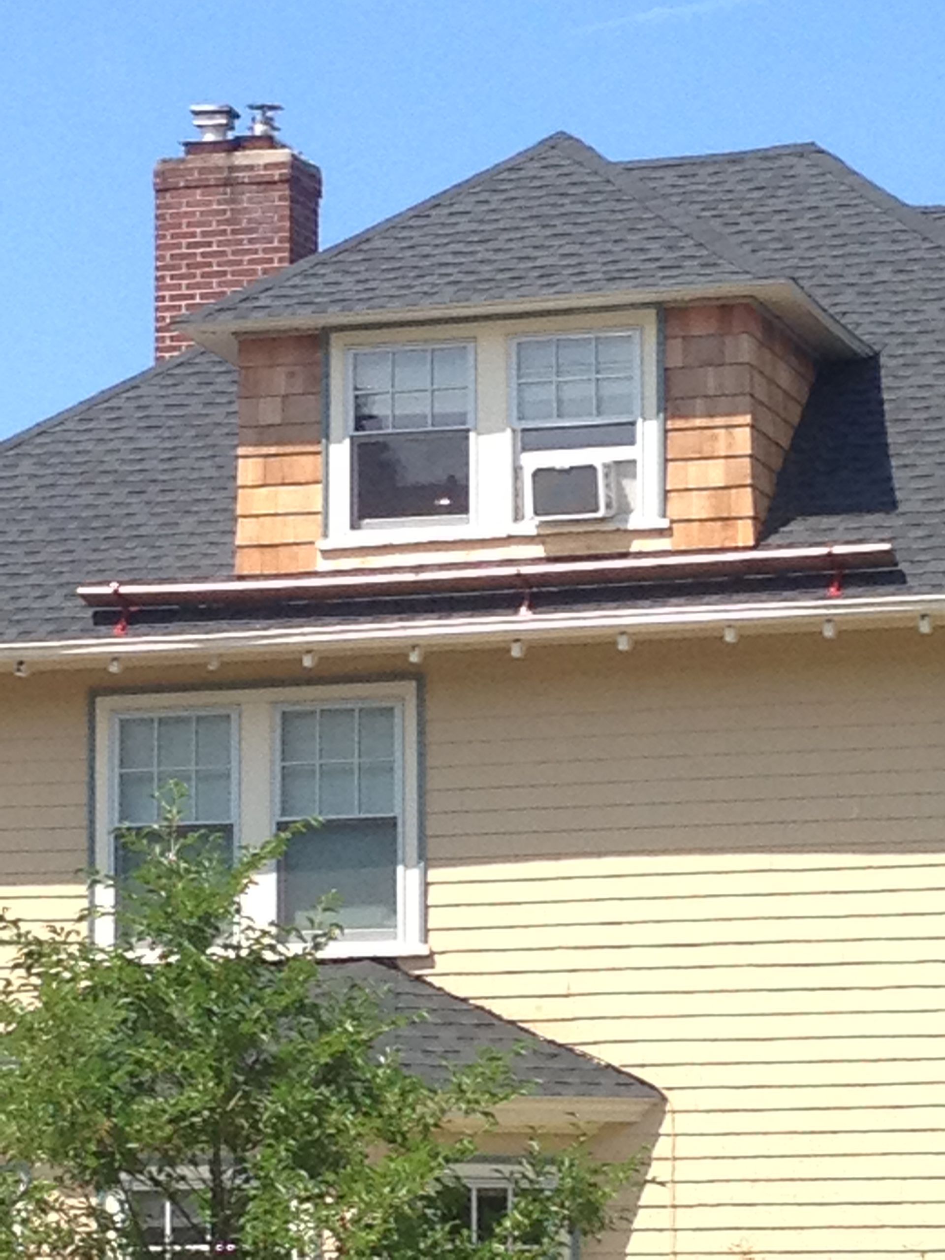 House exterior with tan siding, gray roof, brick chimney, and a dormer window under a blue sky