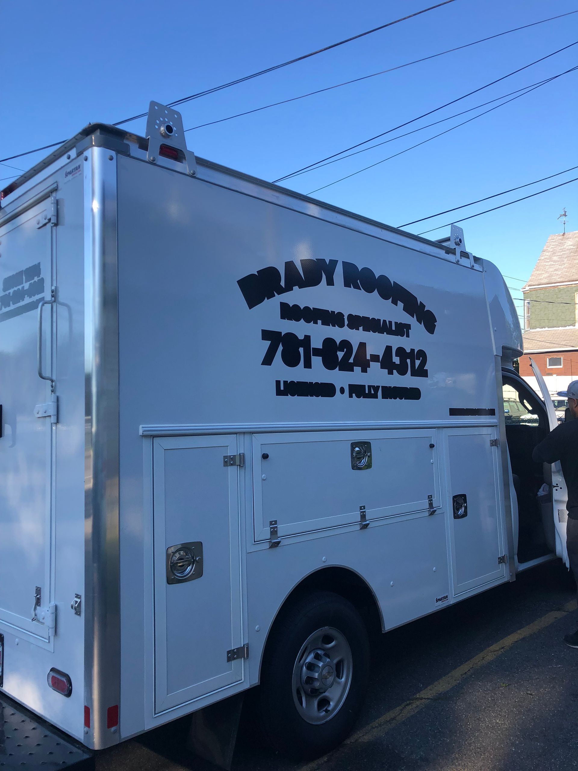 White utility truck with side compartments and black company lettering parked on a street.