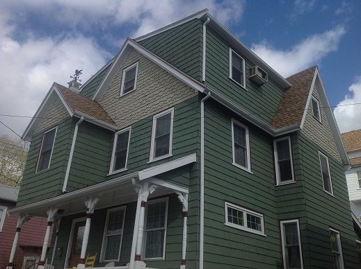 Green house with white trim and a steep roof against a cloudy sky