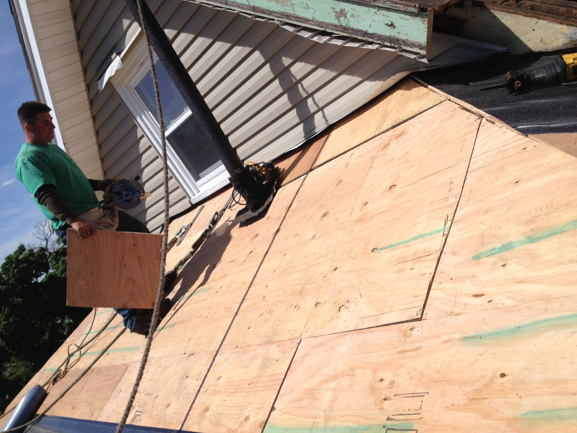 Workers roofing a house with plywood sheathing and ladder on the sloped roof