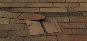Damaged roof shingles with a missing flap exposing the underlayment.
