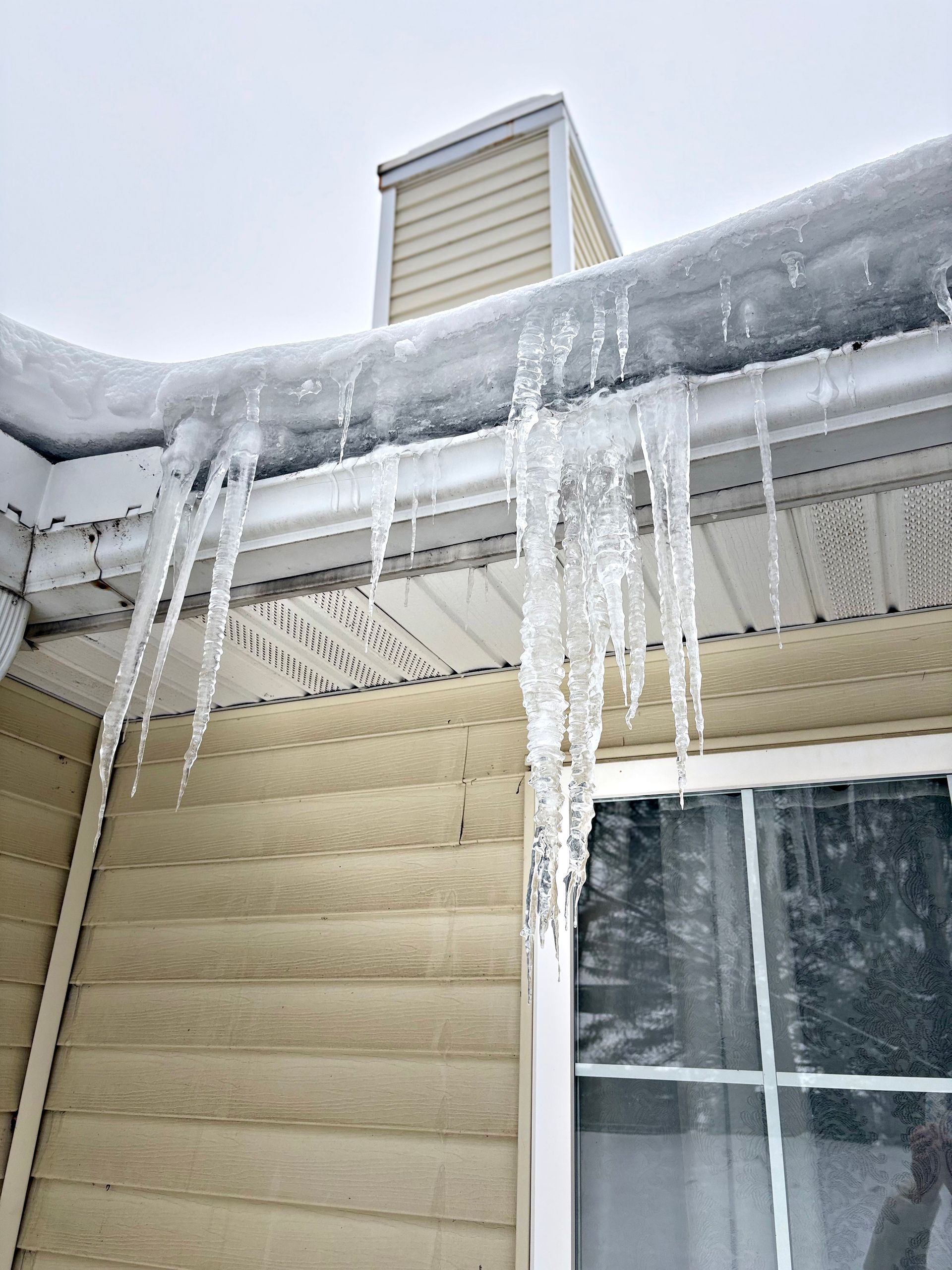 Icicles hanging from a snow-covered roof over a beige house window