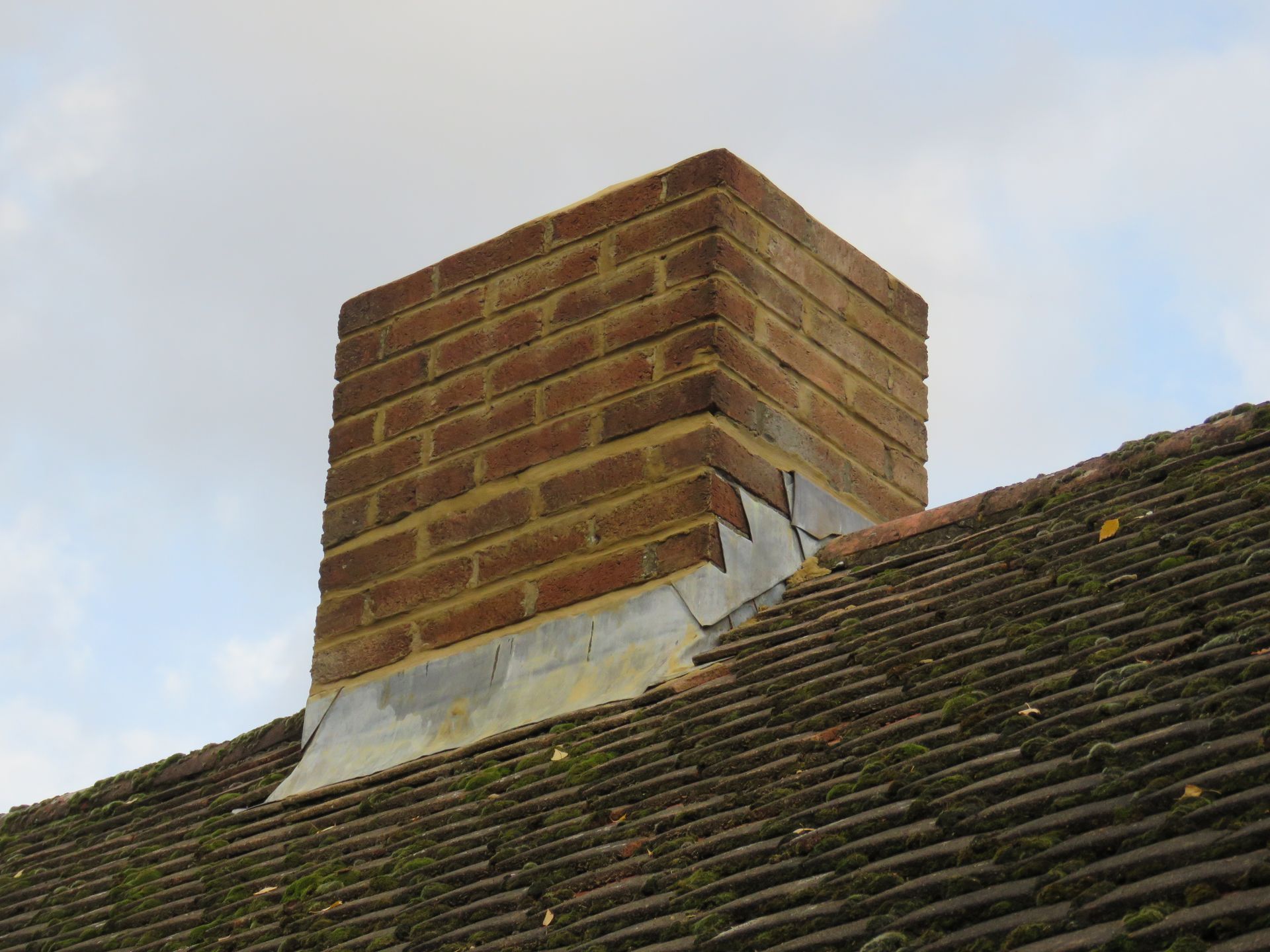 Brick chimney on a tiled rooftop against a cloudy sky
