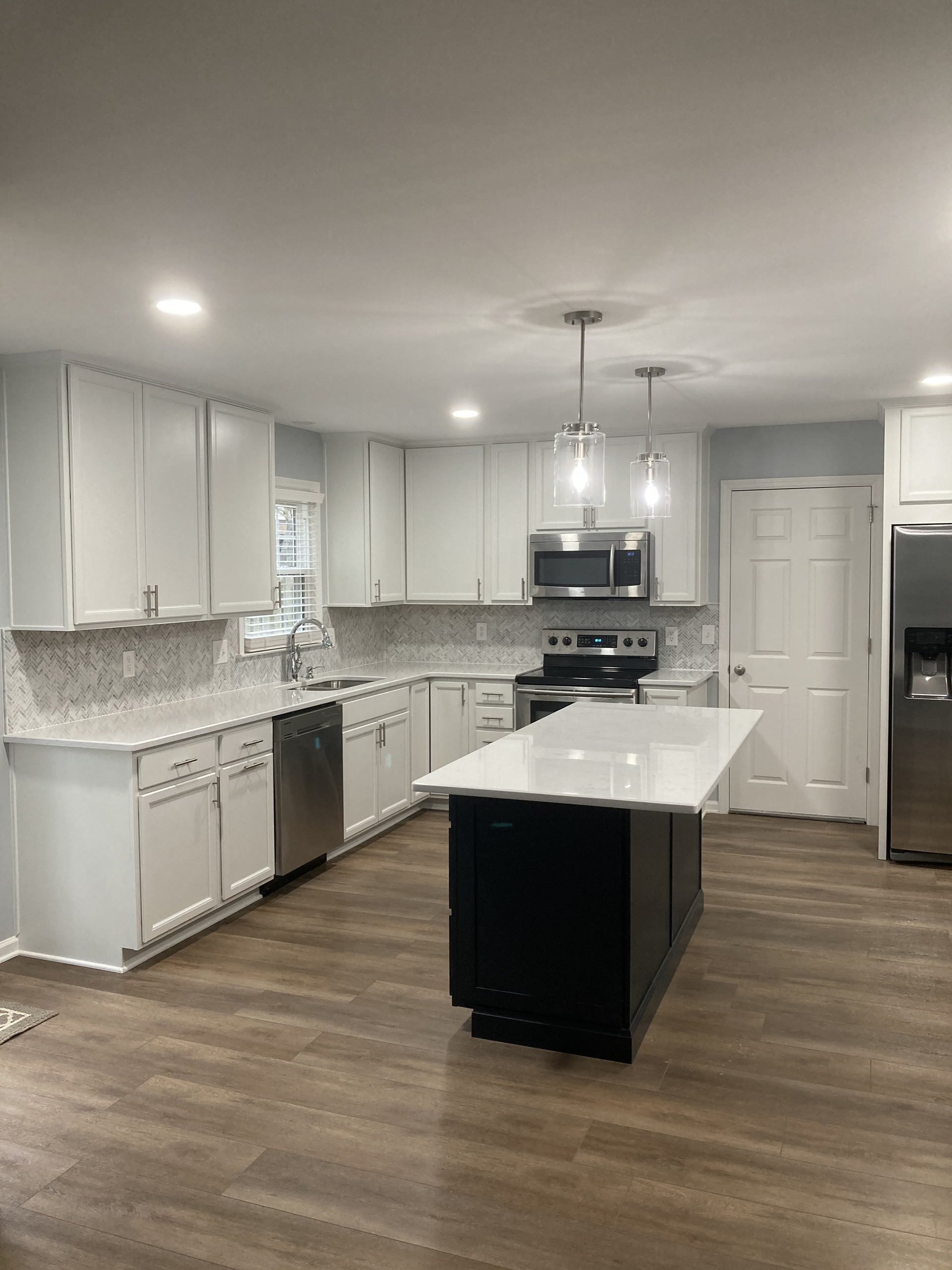 A kitchen with white cabinets , stainless steel appliances , and a large island.