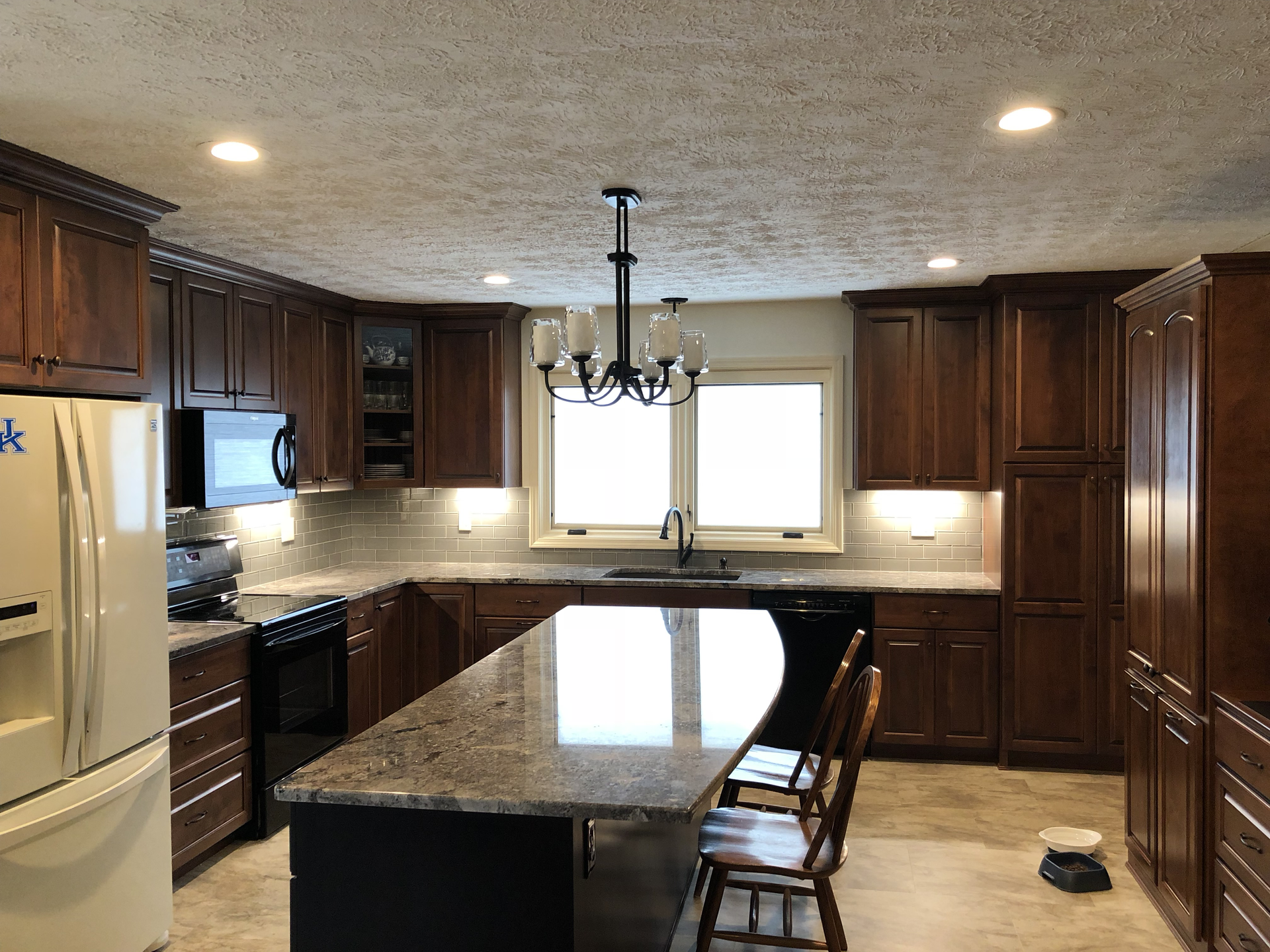 A kitchen with wooden cabinets , granite counter tops , a refrigerator , and a large island.