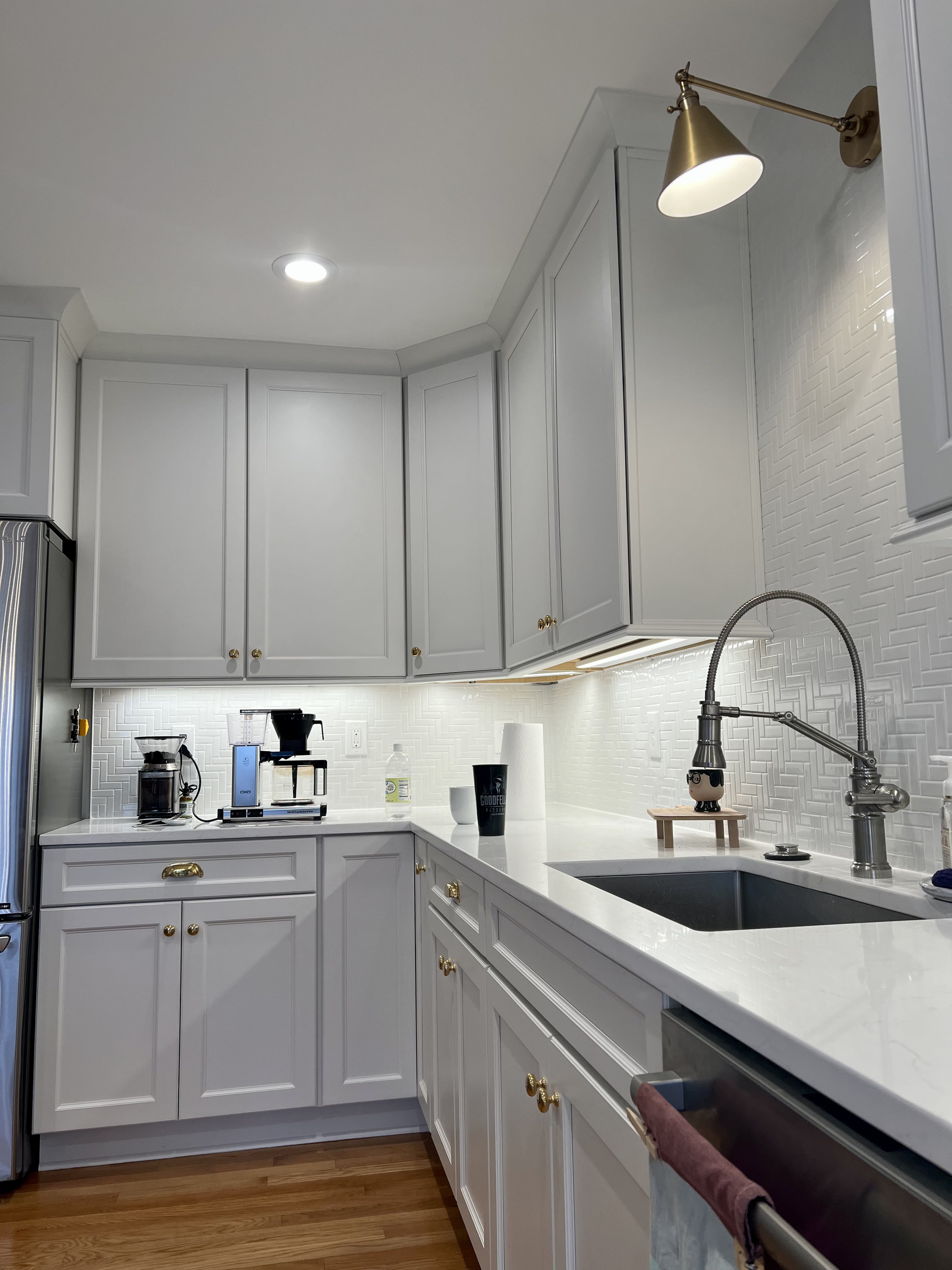 A kitchen with white cabinets , a sink , and a stainless steel refrigerator.