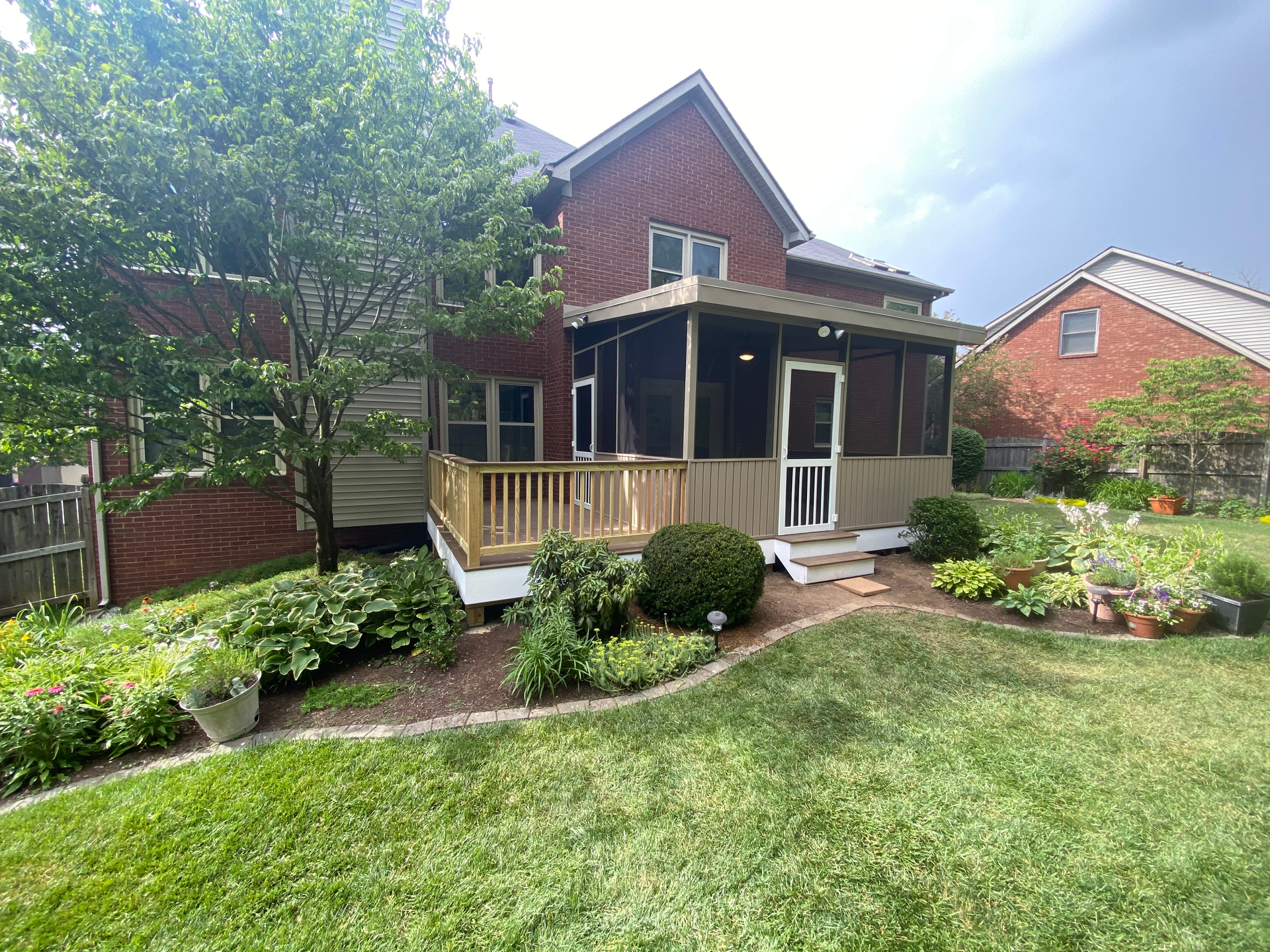 A brick house with a screened in porch and a large lawn in front of it.