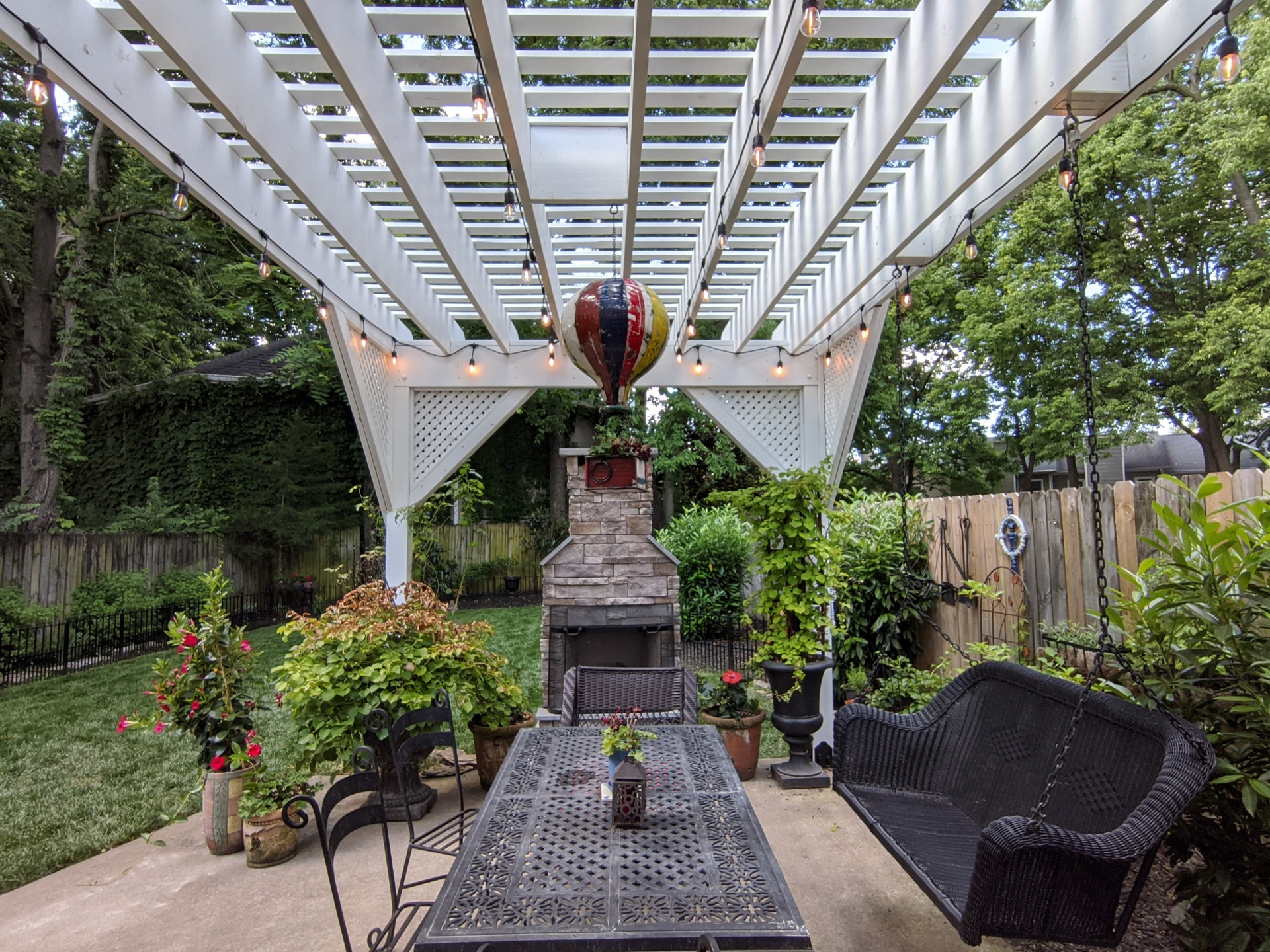 A patio with a table and chairs under a pergola with a hot air balloon hanging from the ceiling.