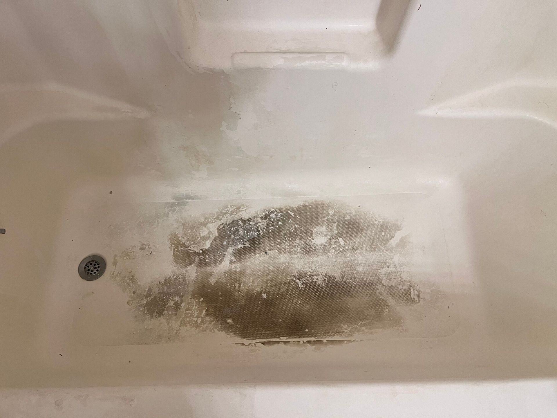 Dirty, off-white bathtub with dark stain in the center, near the drain.