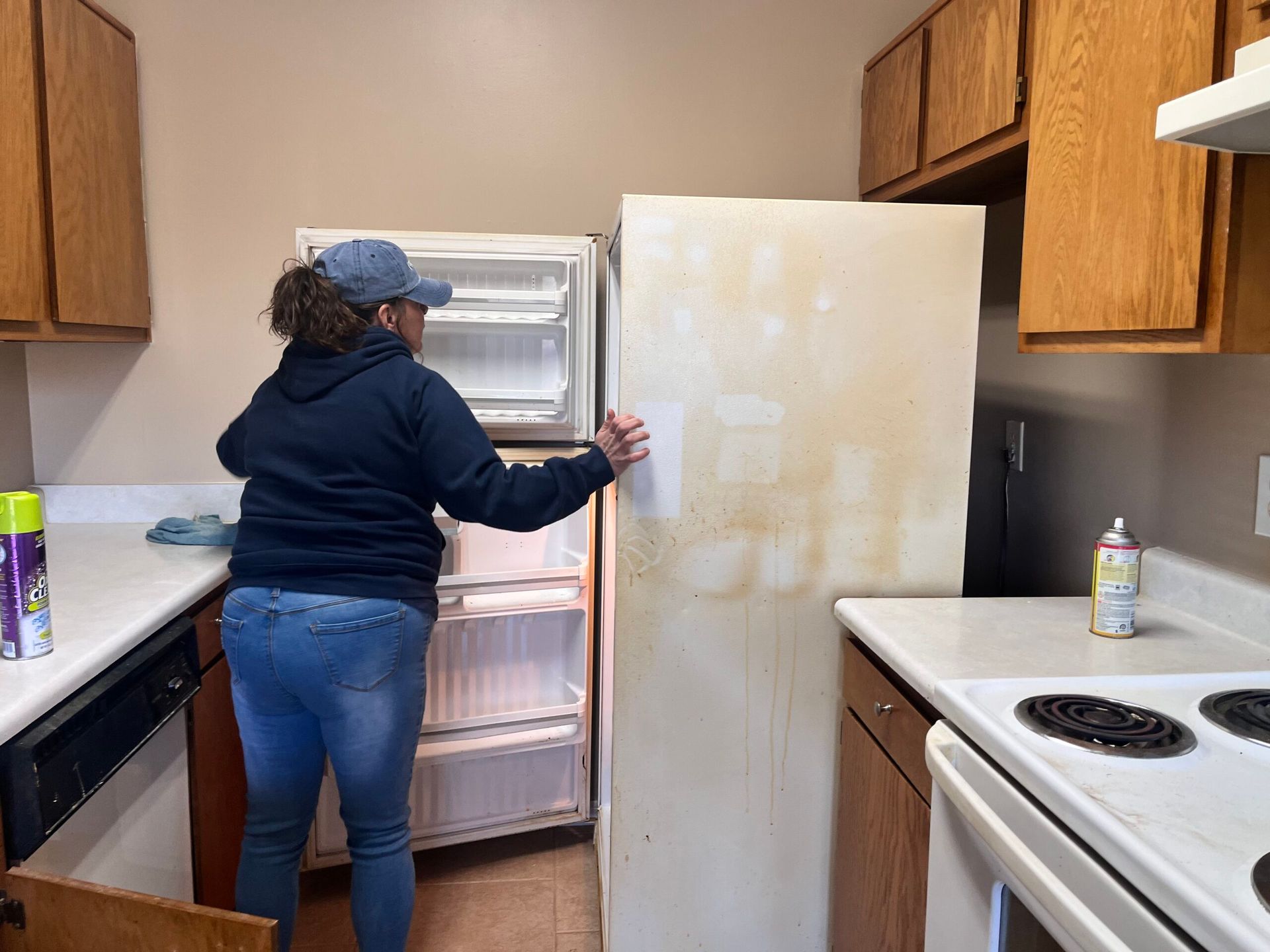 Woman opening a dirty white refrigerator in a kitchen with wooden cabinets.
