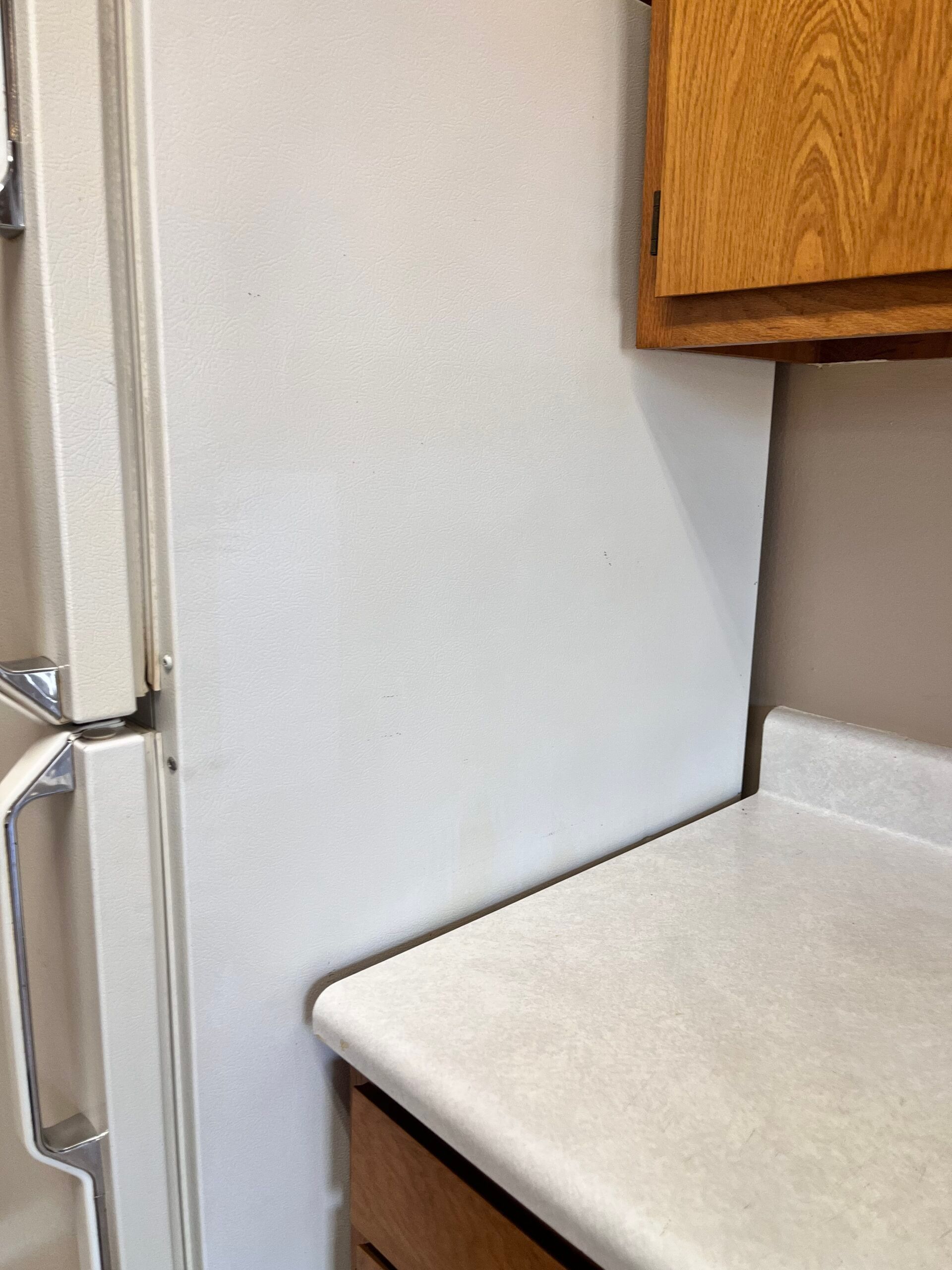 White refrigerator next to a white countertop and wooden cabinet.