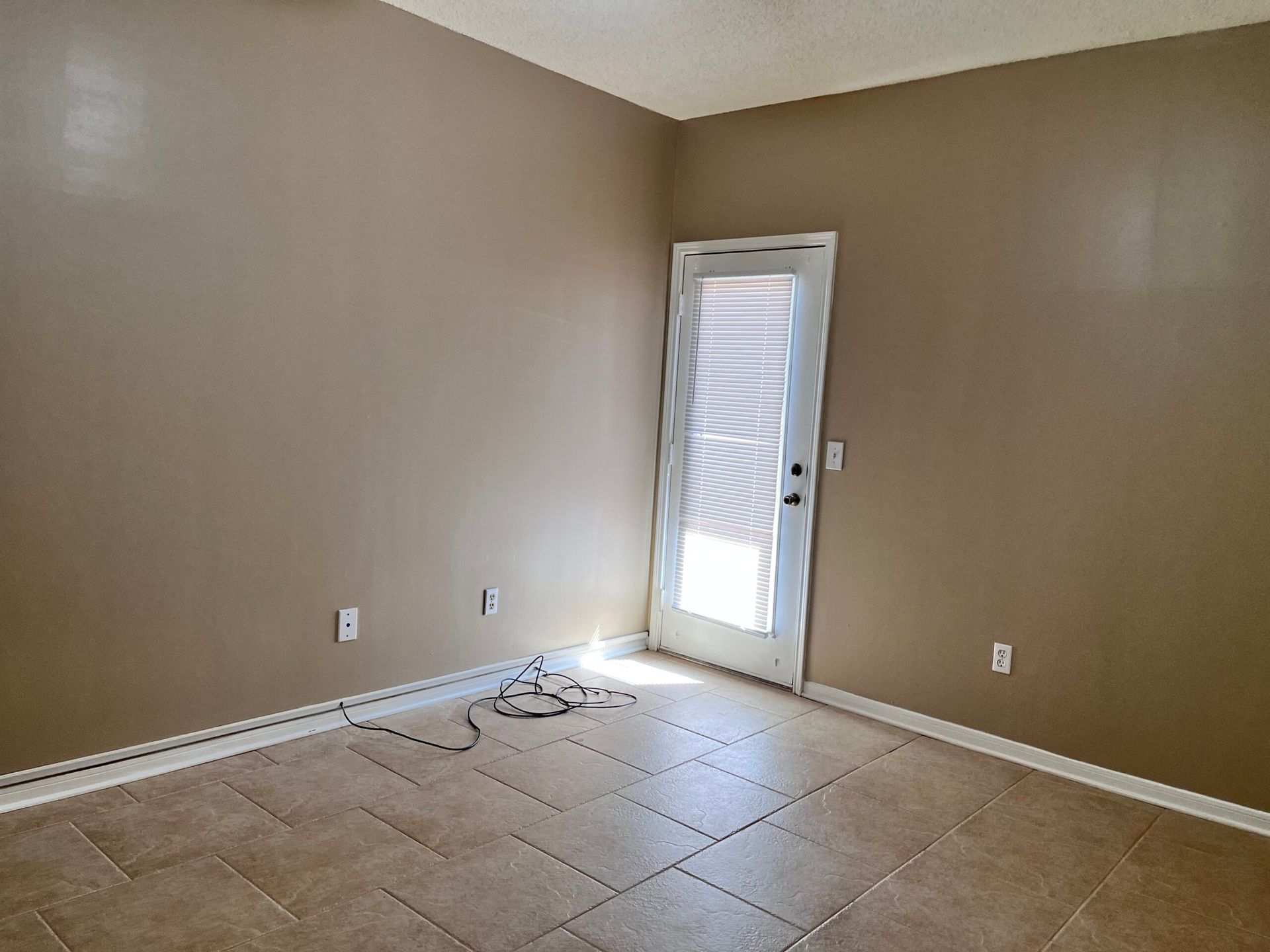 Empty room with beige walls and tile floor, a white door with a screen, and exposed wiring.