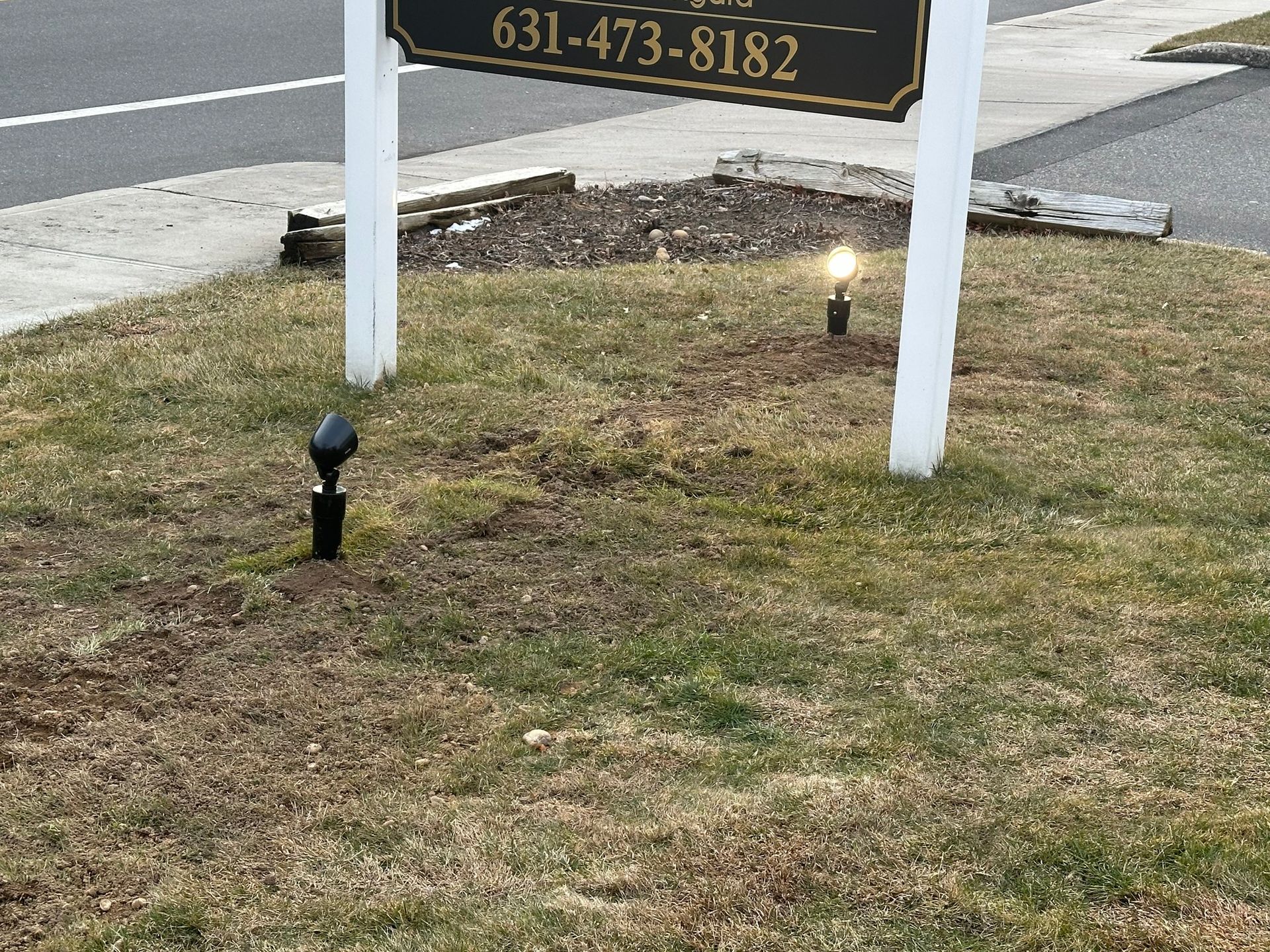 Grassy roadside sign with two small landscape lights and a black sprinkler head in front