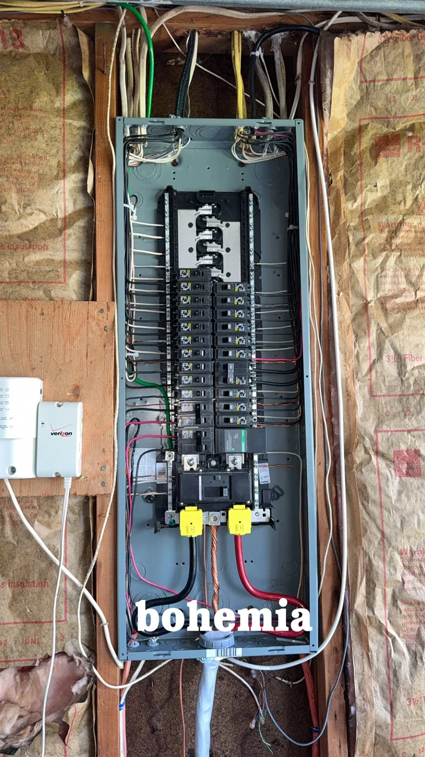 Electrical breaker panel in an unfinished wall, with exposed wiring and labeled circuits.