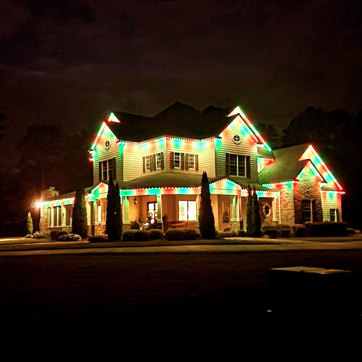House decorated with green, red, and white Christmas lights at night.