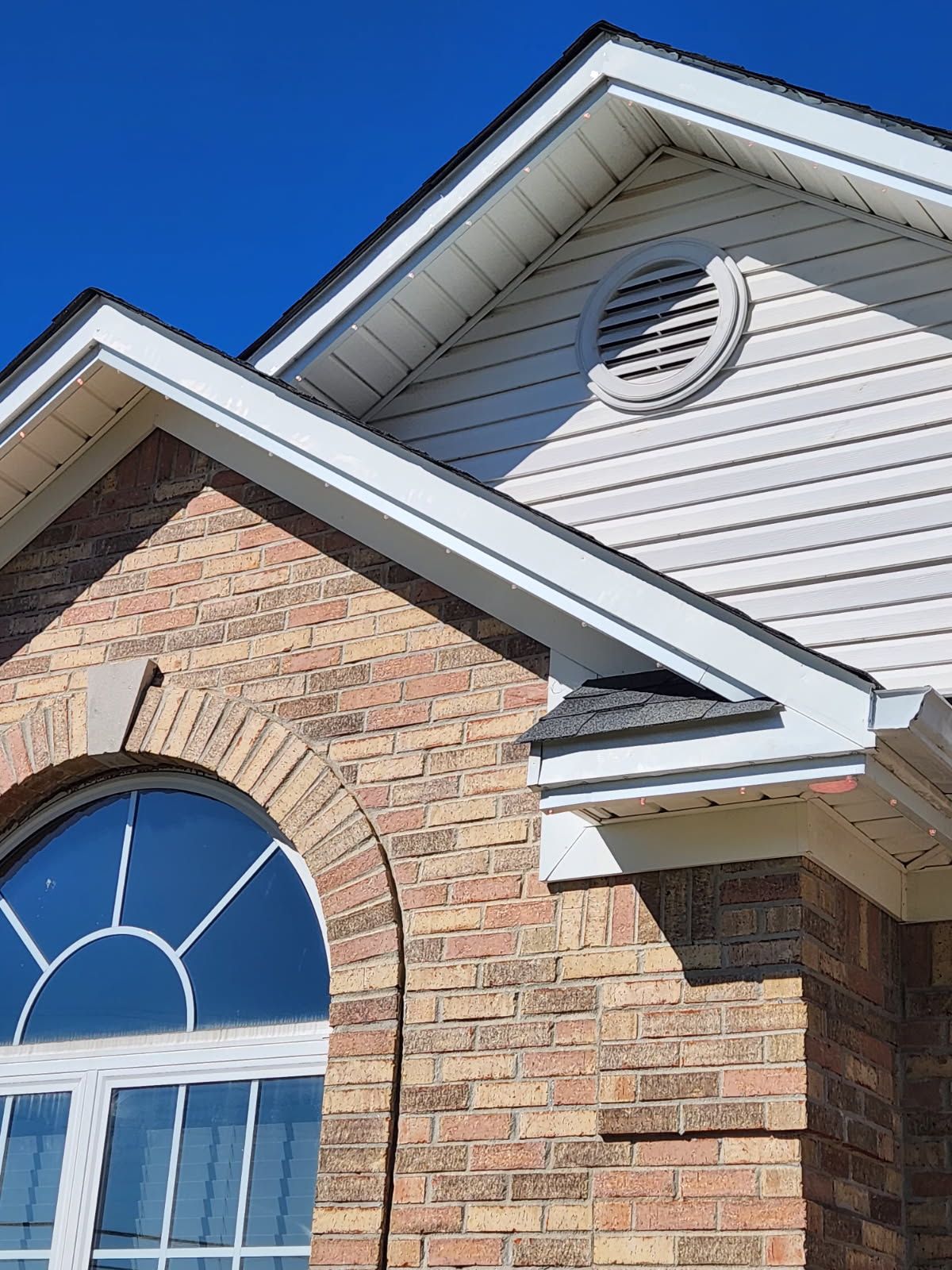 Brick house exterior with arched window, white trim, and blue sky.