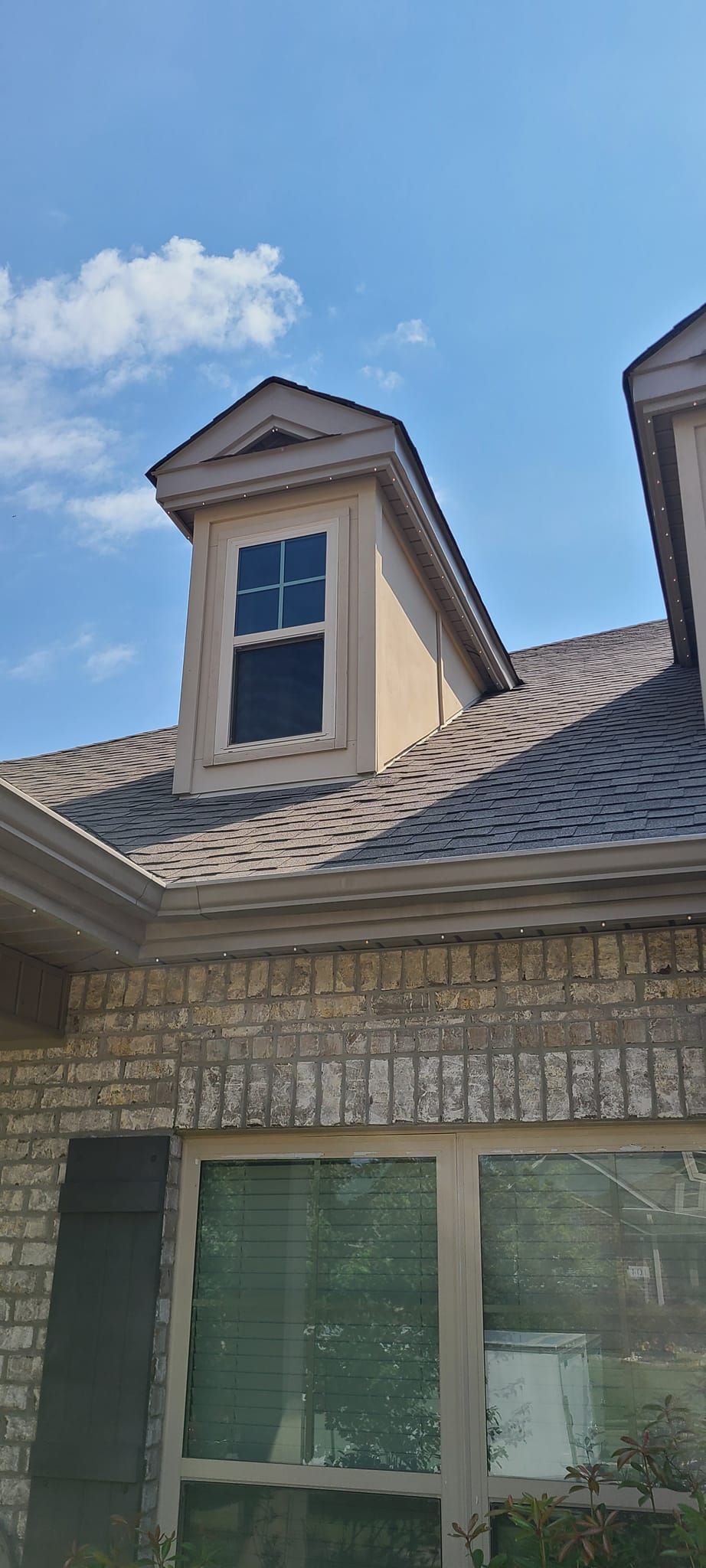 A house with a dormer window, brick facade, and brown roof tiles against a blue sky.