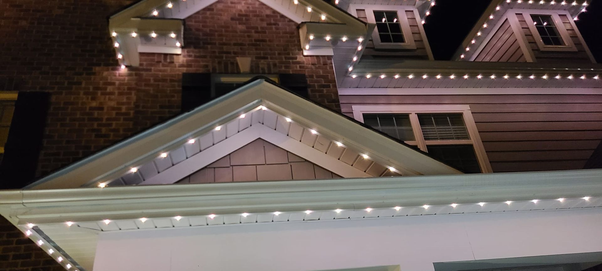 House roof with white lights along the edges; dark brick and wood siding visible.