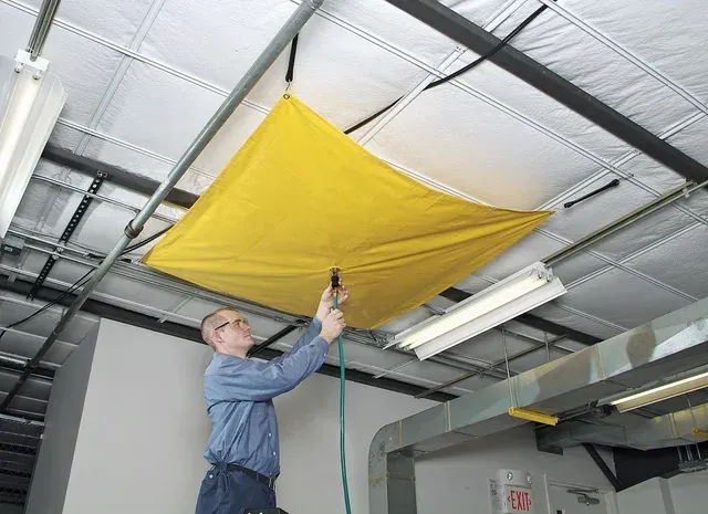 A man is working on a ceiling with a yellow tarp.