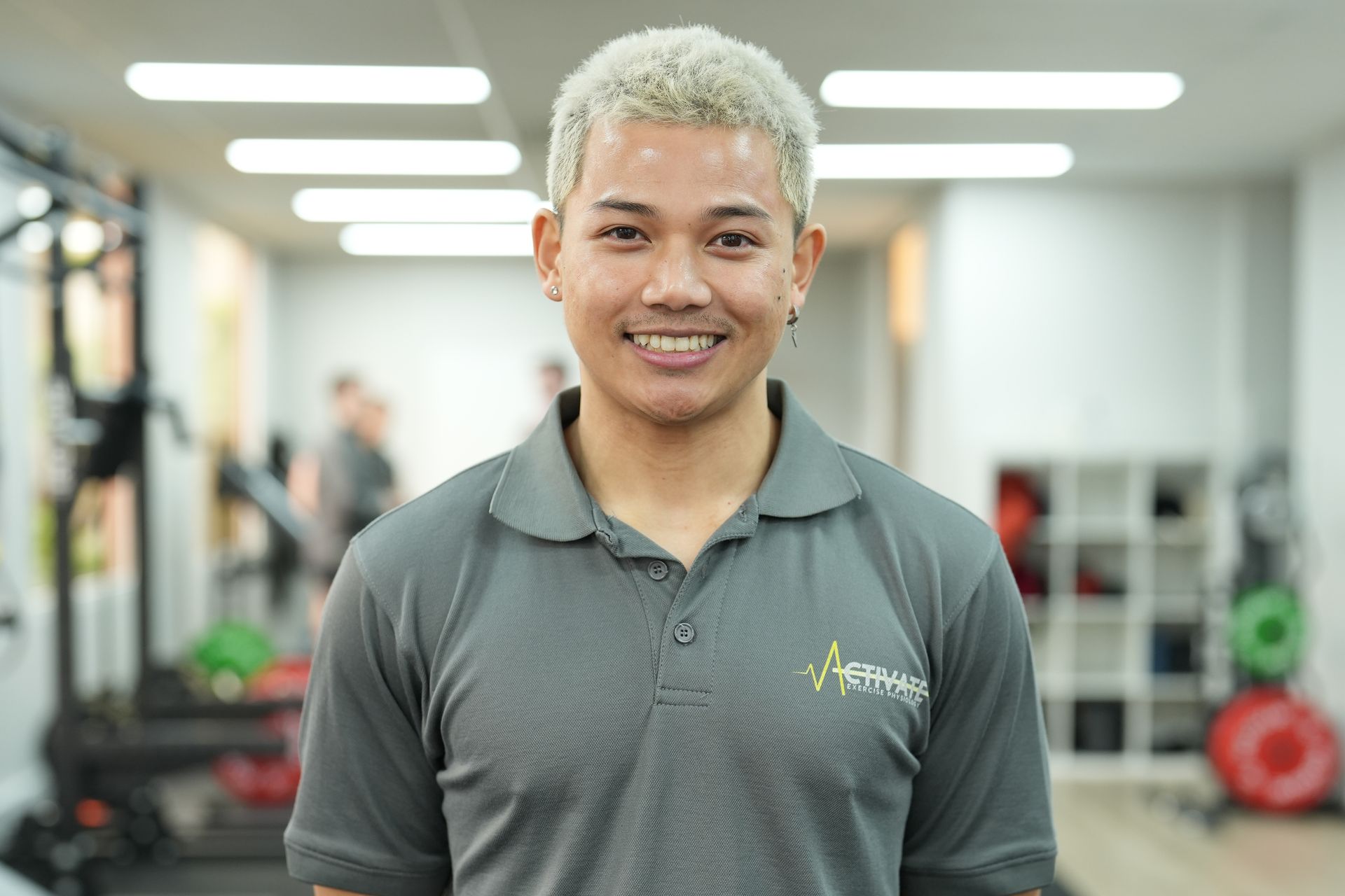 A man in a grey polo shirt is smiling in a gym.