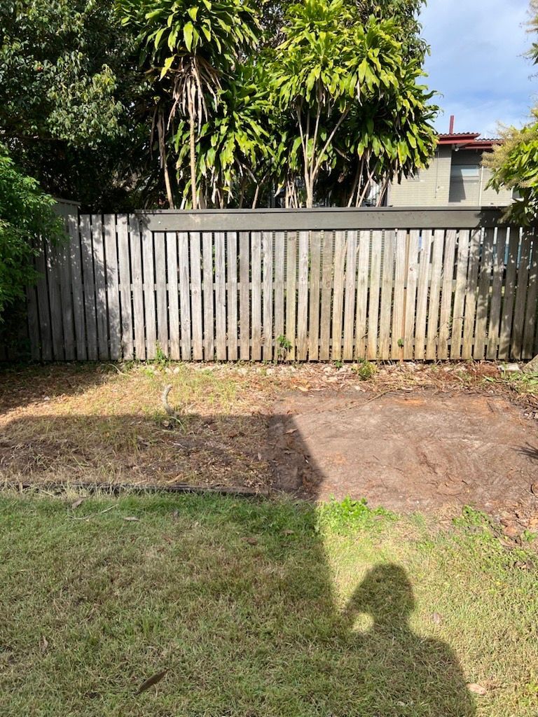 Backyard with weathered wooden fence, brown patches of soil and grass. A person's shadow is cast on the grass — Rob's Rubbish Removal in Byron Bay, NSW