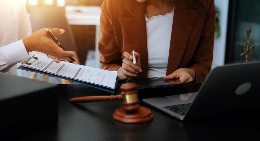 Hands signing a legal document beside a gavel and laptop in a lawyer’s office
