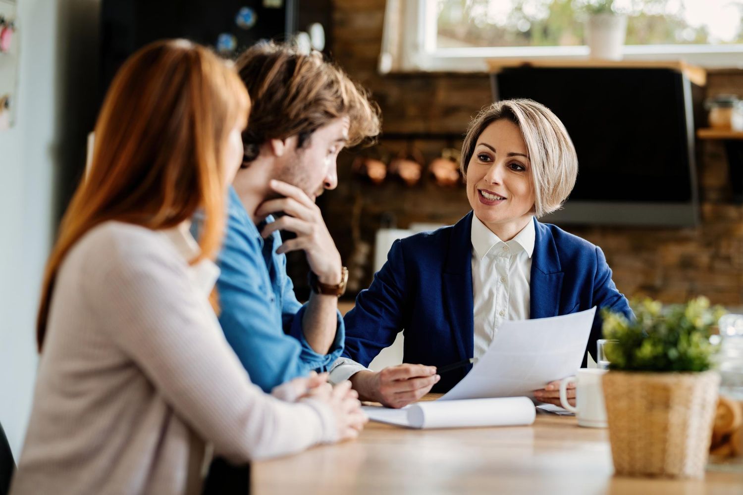 Three coworkers discuss documents at a table in a warm office or café setting.