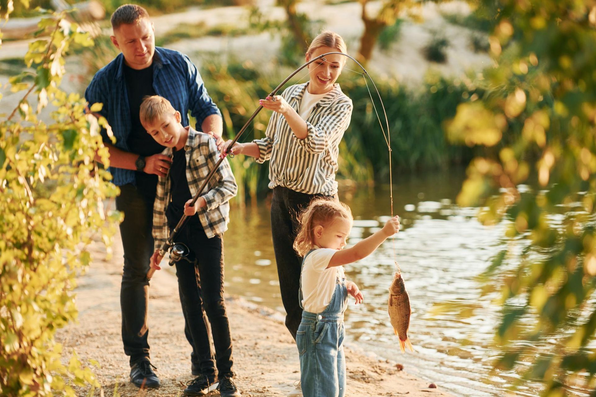 Family fishing by a pond on a sunny day, with a child holding up a caught fish.