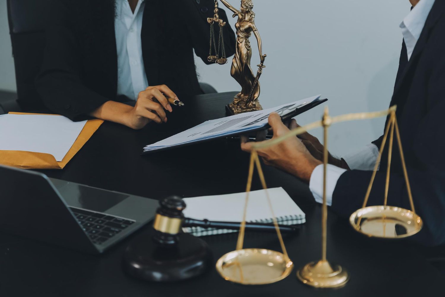 Business meeting at a desk with a laptop, papers, gavel, and gold scales of justice.