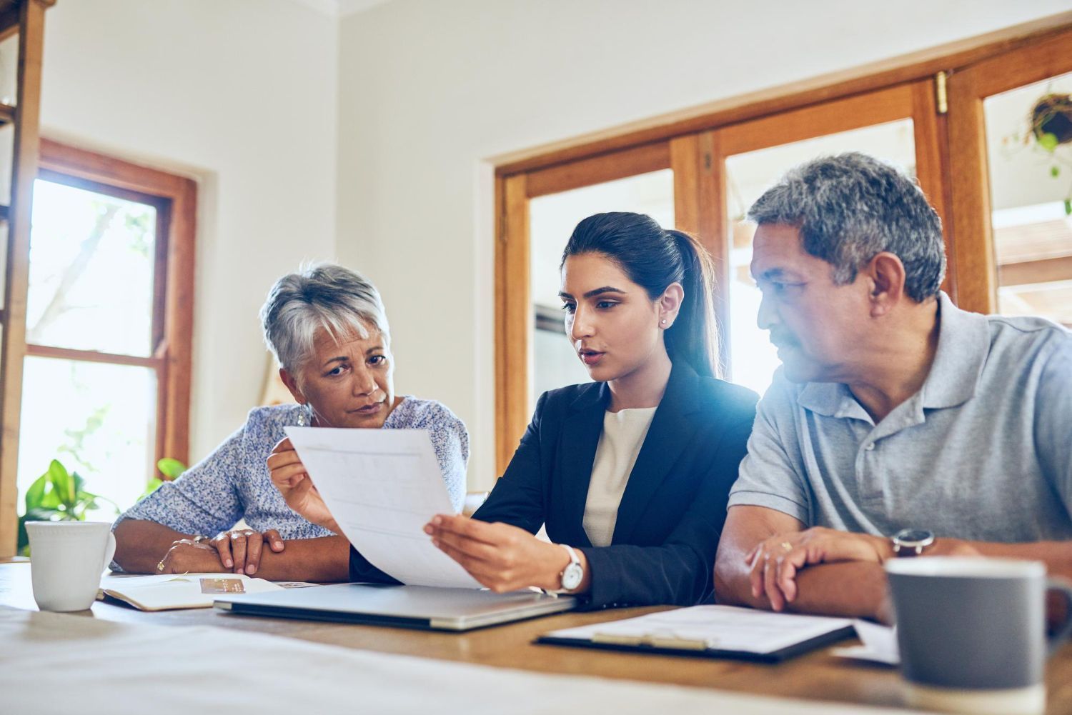 Three people review documents at a table in a bright office meeting room.