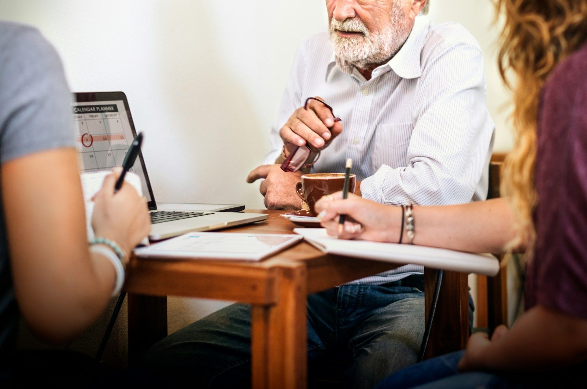 People in a meeting around a table, one person gesturing while others take notes.