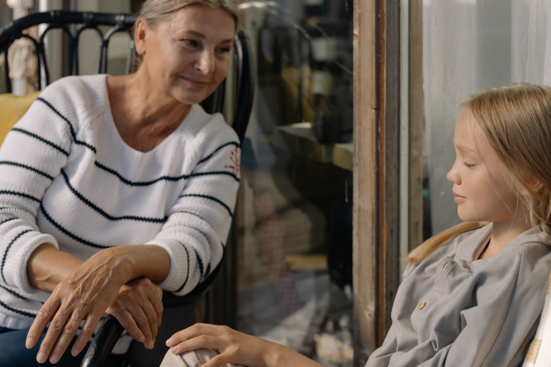 Woman talking with a child by a window, both seated and facing each other.