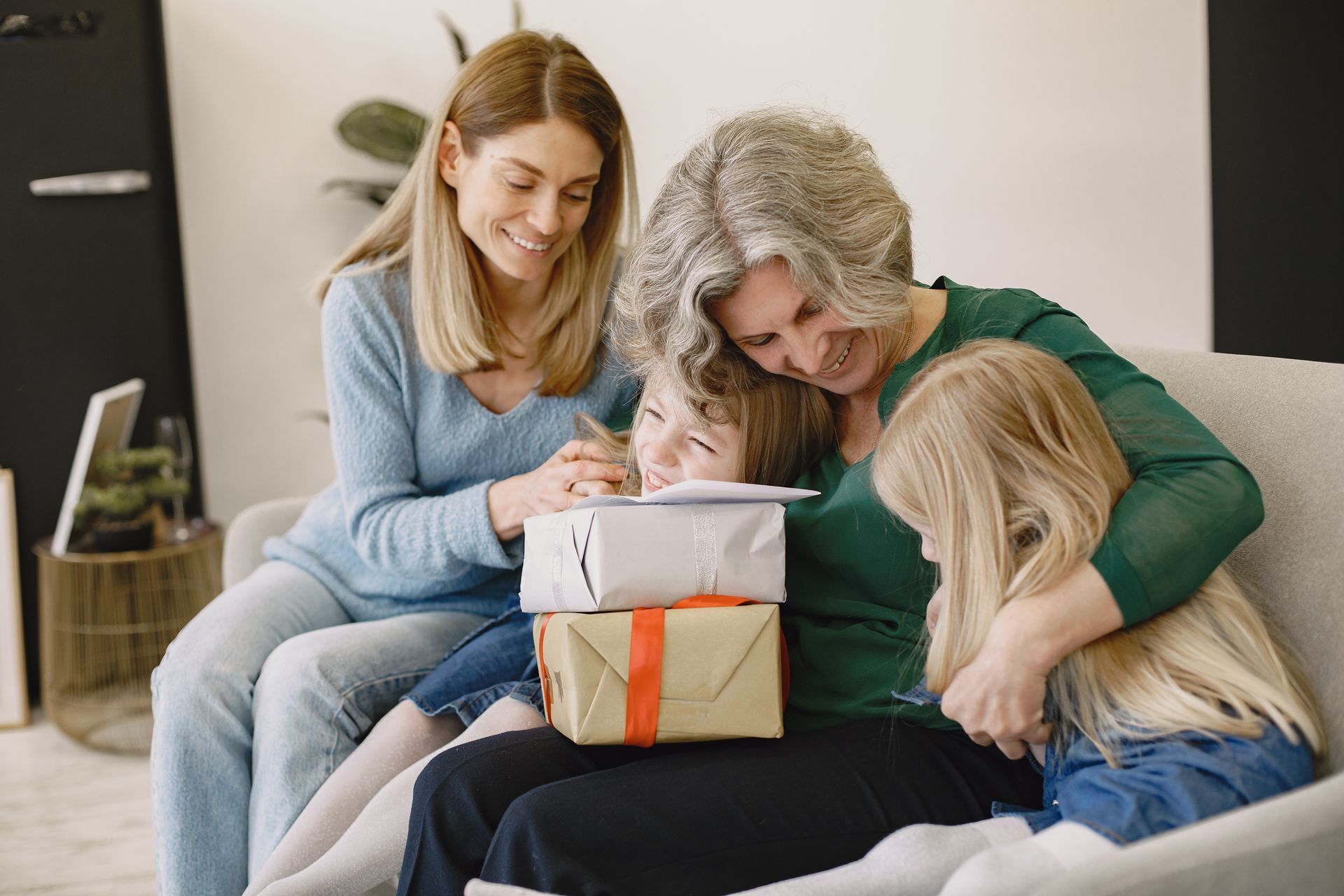 Four people on a couch smiling as they open a wrapped gift together