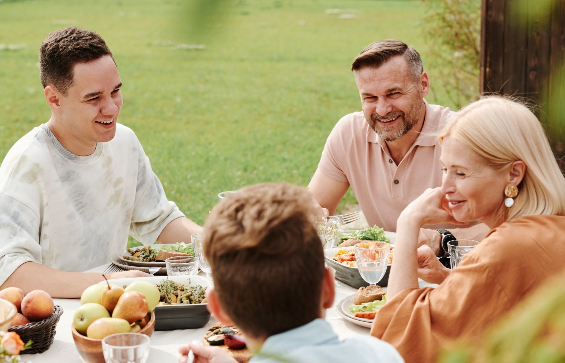Friends sharing a meal outdoors at a picnic table, smiling in a sunny garden.