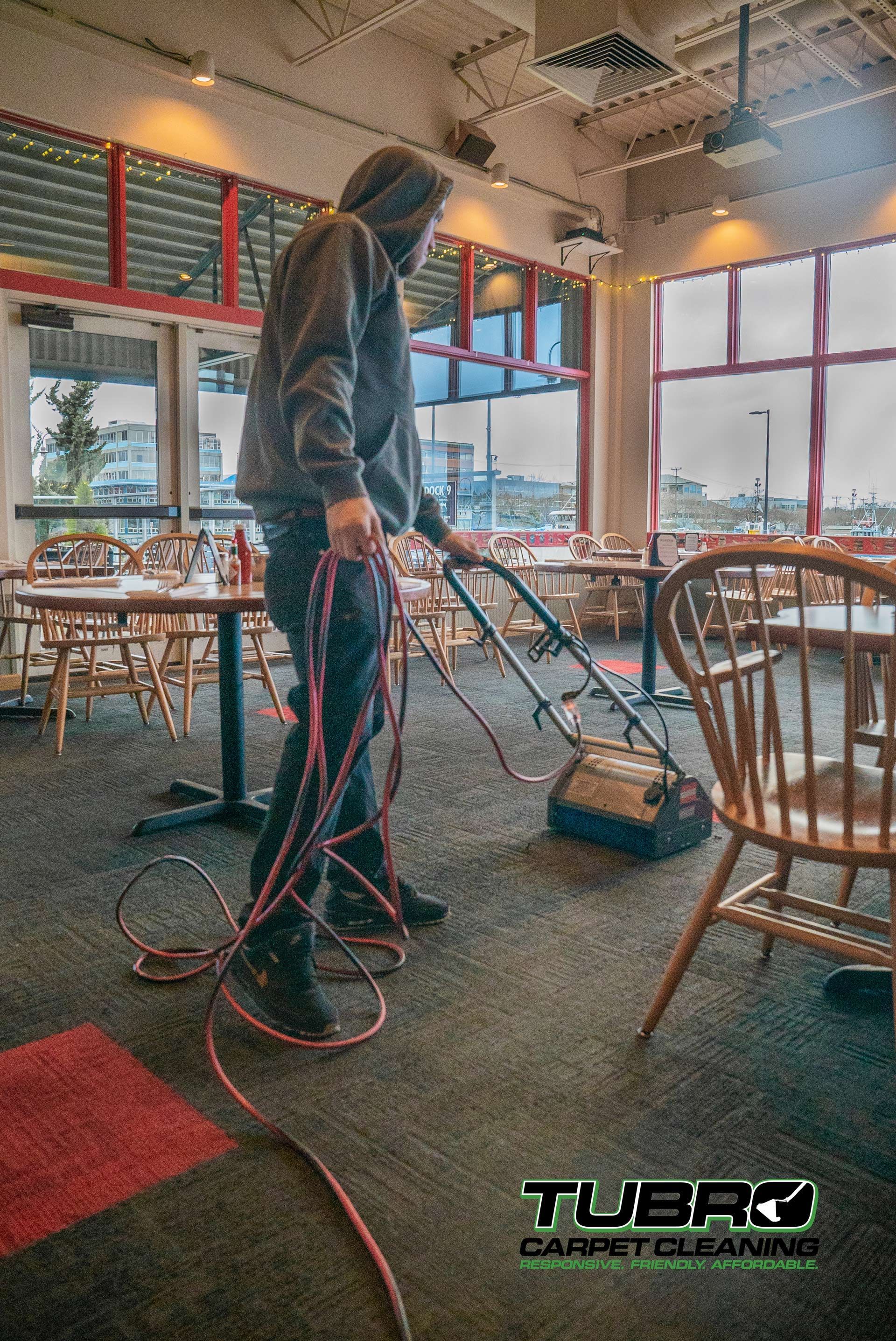 A man is cleaning the carpet in a restaurant with a vacuum cleaner.