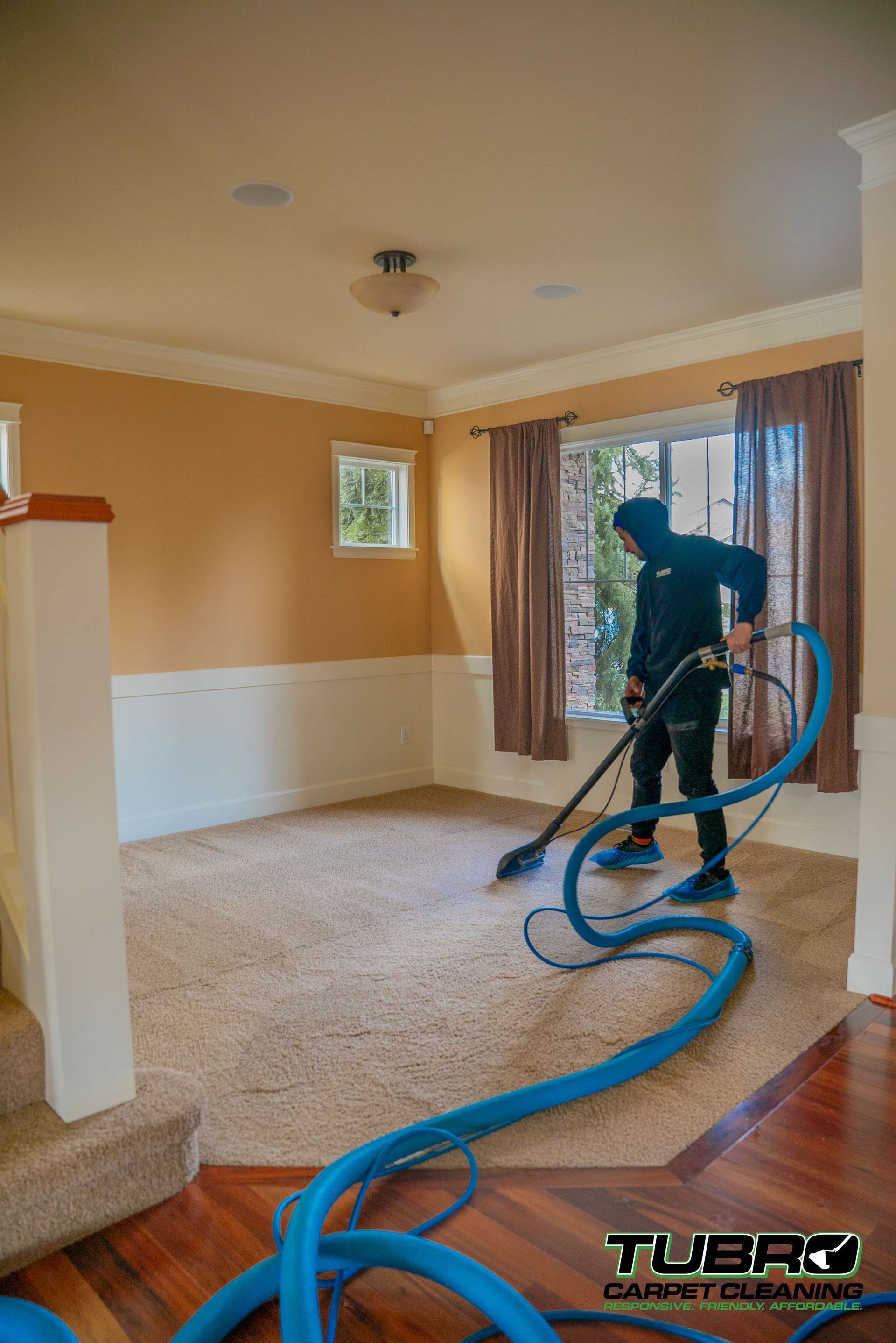A man is cleaning a carpet in a living room with a vacuum cleaner.