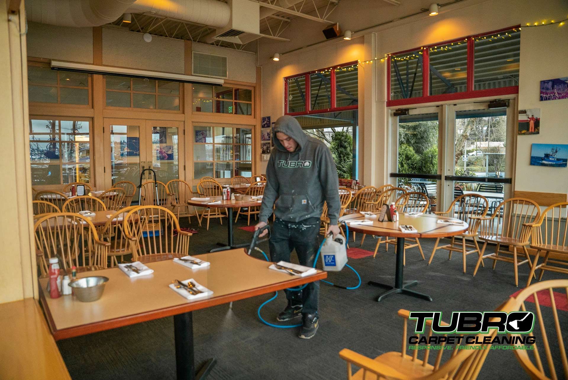 A man in a hoodie is spraying tables in a restaurant.
