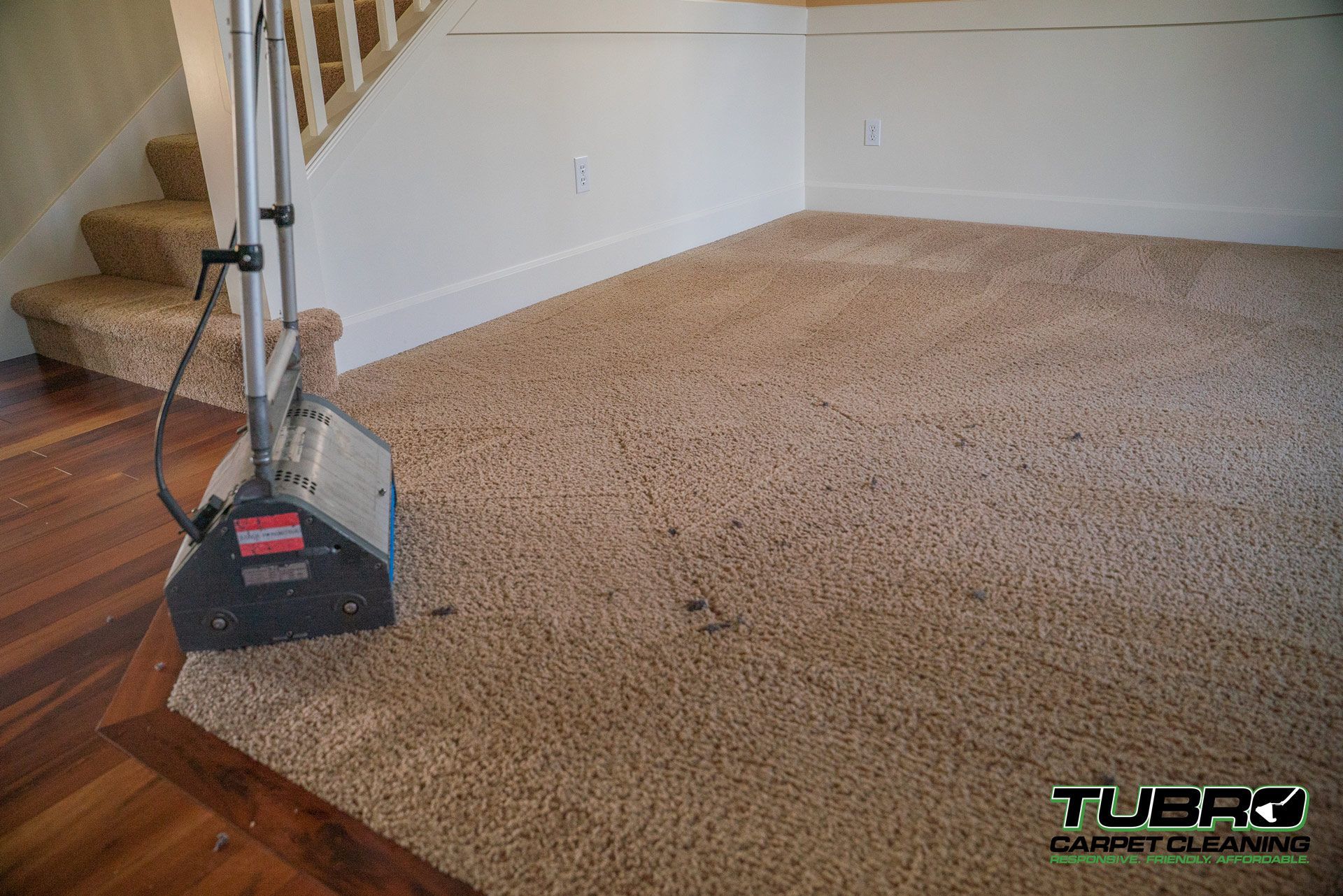 A carpet cleaner is sitting on a carpet in a living room next to stairs.