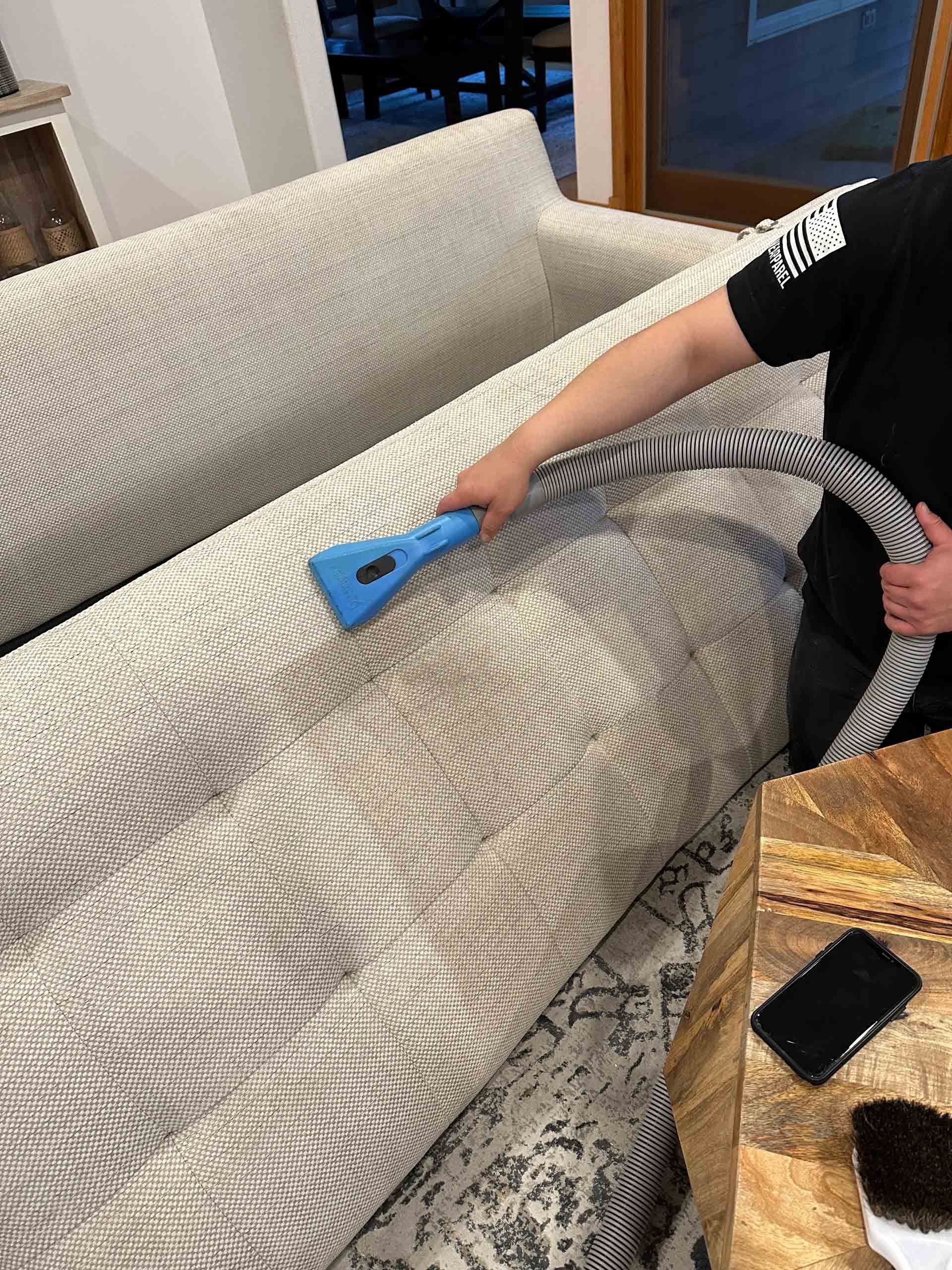 A man is cleaning a couch with a vacuum cleaner.