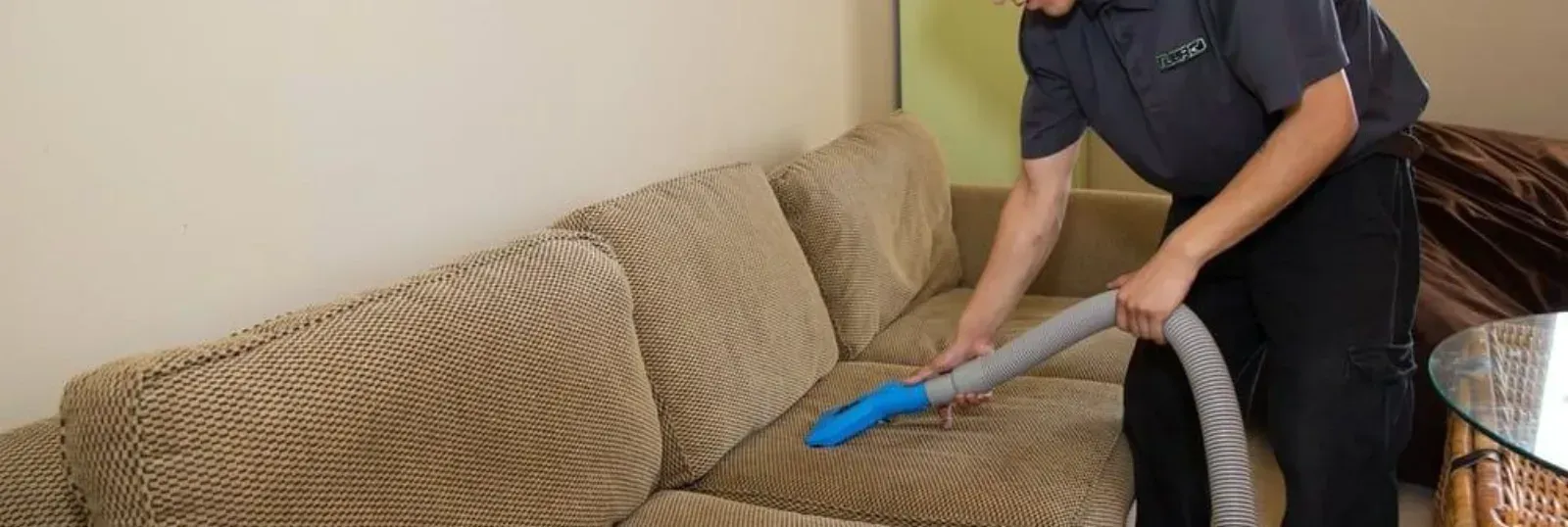 Professional upholstery cleaning technician using an extraction tool on a fabric sofa