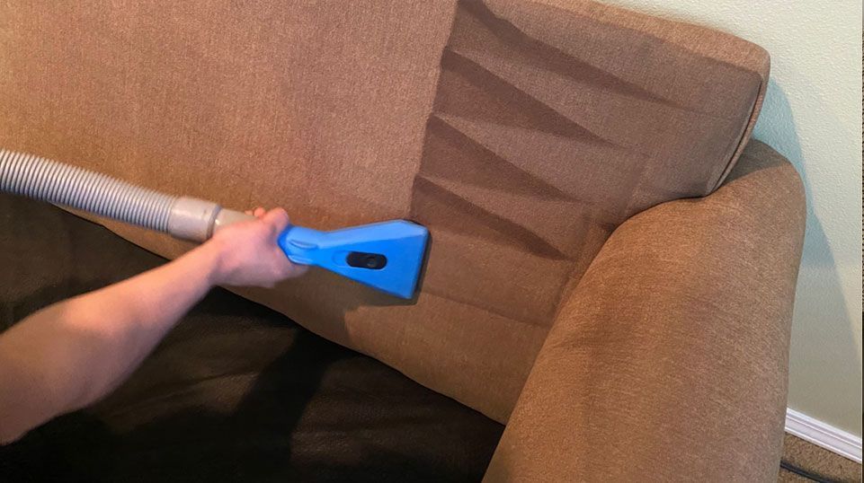 A person is cleaning a couch with a vacuum cleaner.